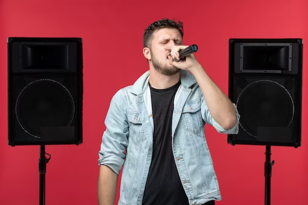 Front view of male singer performing on stage with stereo system on red wall