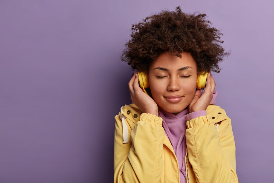 Woman with short hair, eyes closed, listening to headphones on a purple background