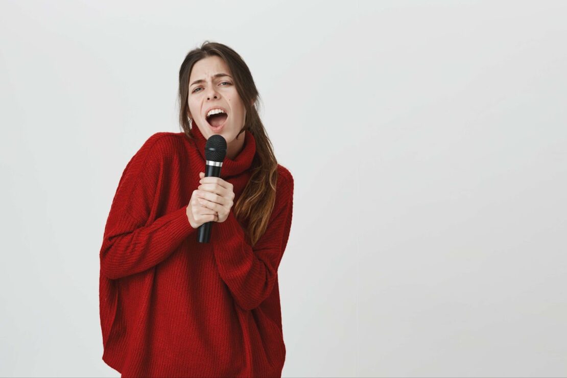 A woman in a red sweater sings into a microphone